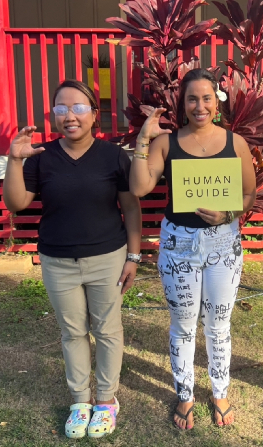 Two participants smiling at the camera, with human guide signage, awareness glasses and making the letter C with their right hands.